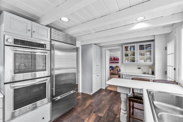 kitchen with stainless steel appliances, white cabinets, light countertops, beam ceiling, and glass insert cabinets