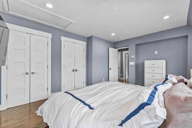 bedroom featuring wood finished floors, two closets, attic access, and recessed lighting