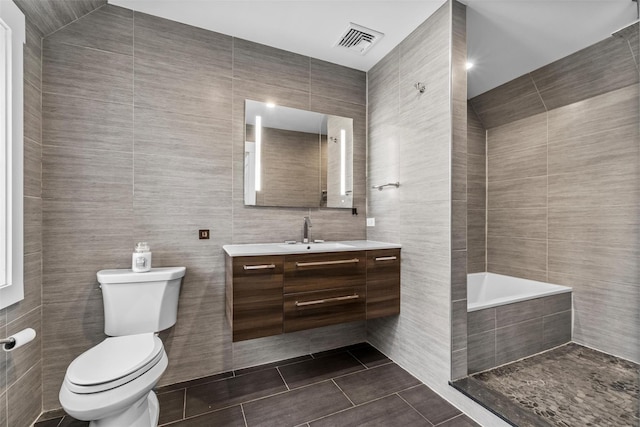 full bathroom featuring toilet, vanity, visible vents, tile walls, and tile patterned floors