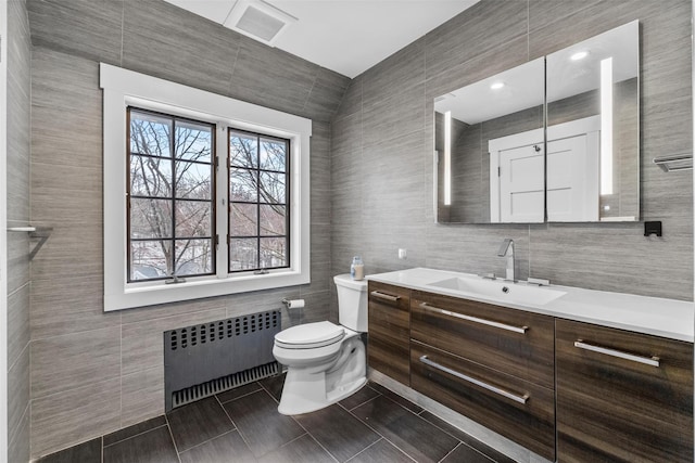 bathroom featuring toilet, visible vents, vanity, tile walls, and radiator heating unit