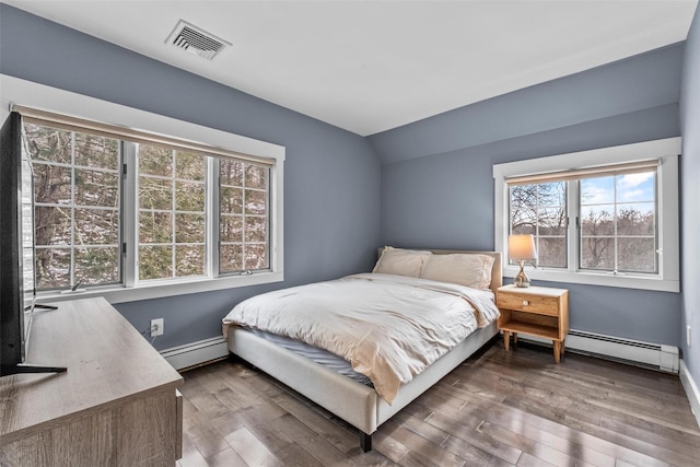 bedroom featuring a baseboard heating unit, wood finished floors, and visible vents