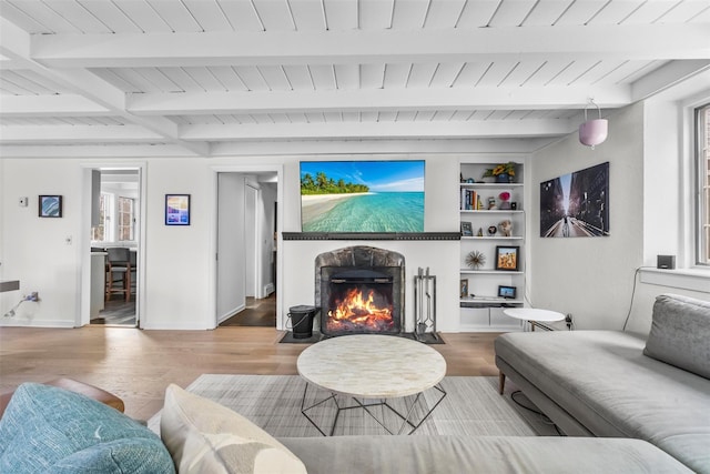 living area featuring built in shelves, a fireplace with flush hearth, wood finished floors, baseboards, and beam ceiling