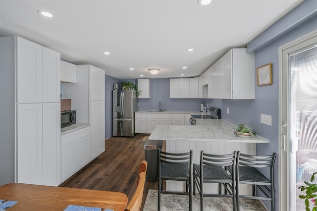 kitchen with appliances with stainless steel finishes, dark hardwood / wood-style floors, white cabinetry, a kitchen breakfast bar, and kitchen peninsula