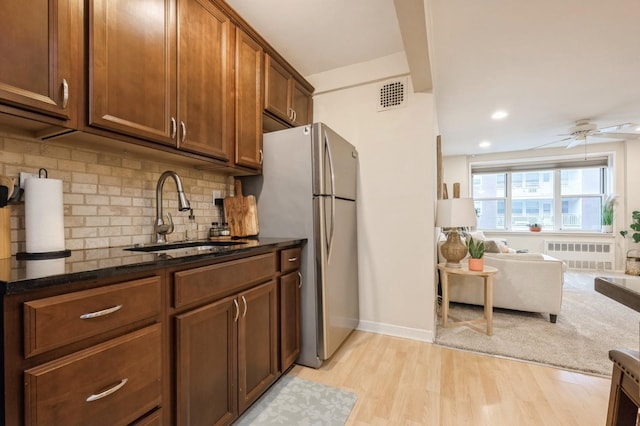 kitchen with radiator heating unit, sink, dark stone countertops, backsplash, and light hardwood / wood-style floors