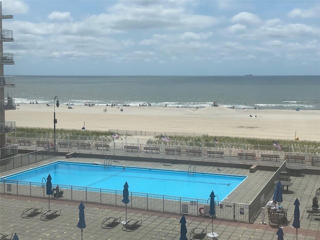 view of pool featuring a patio, a beach view, and a water view