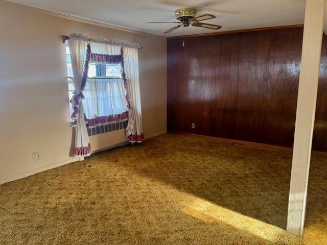 spare room with carpet flooring, radiator, ceiling fan, and wood walls