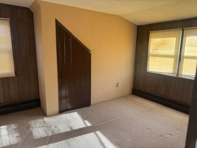 carpeted empty room with vaulted ceiling, a baseboard heating unit, and wooden walls