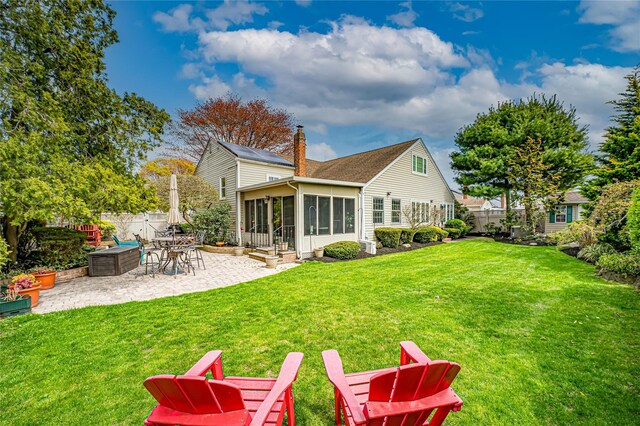 rear view of house with a chimney, a lawn, a sunroom, fence, and a patio