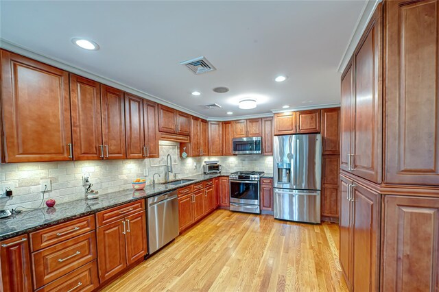 kitchen featuring appliances with stainless steel finishes, a sink, dark stone counters, light wood-type flooring, and visible vents