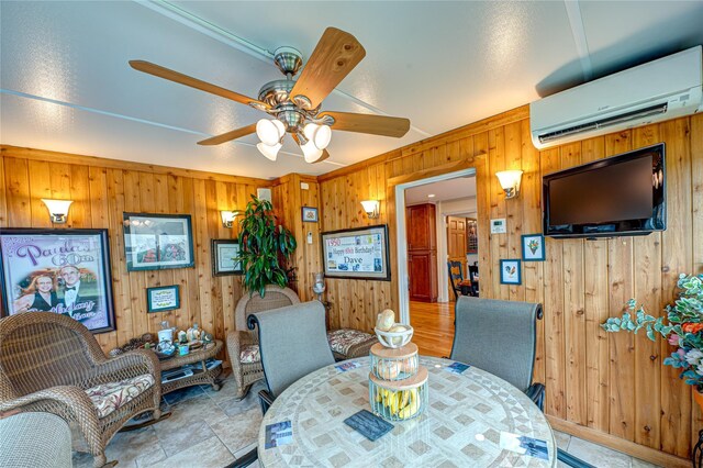 dining space featuring an AC wall unit, a ceiling fan, wooden walls, and stone finish floor