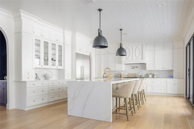 kitchen featuring white cabinetry, light wood-type flooring, an island with sink, and built in refrigerator