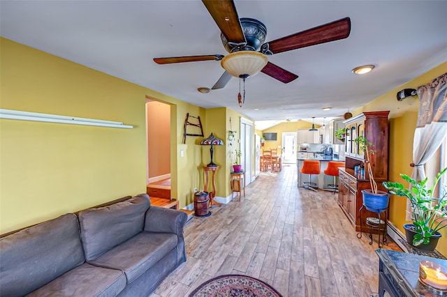 living area featuring a ceiling fan, light wood-style flooring, and baseboards