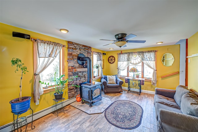 living room featuring a wood stove, a healthy amount of sunlight, baseboard heating, and wood finished floors