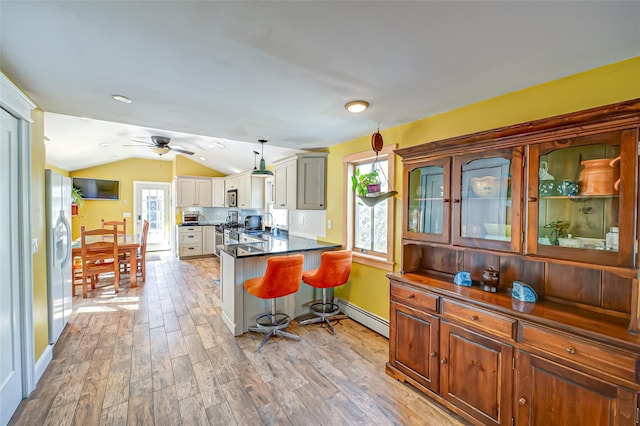 kitchen featuring baseboard heating, vaulted ceiling, light wood-type flooring, a peninsula, and a kitchen bar