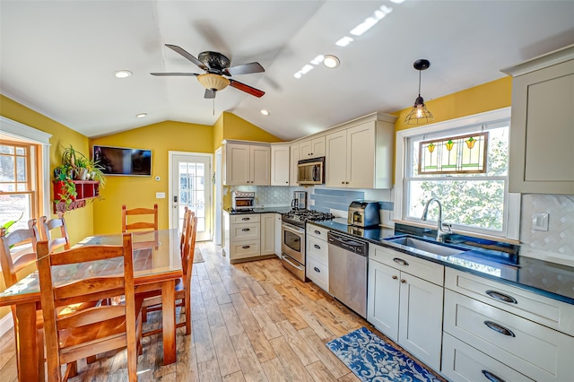 kitchen with dark countertops, light wood-style flooring, appliances with stainless steel finishes, vaulted ceiling, and a sink