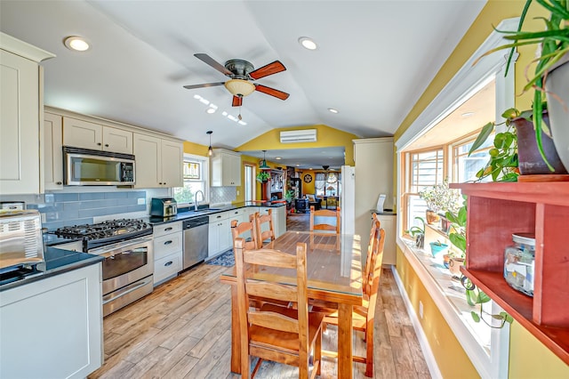 kitchen with stainless steel appliances, dark countertops, a wealth of natural light, vaulted ceiling, and a sink