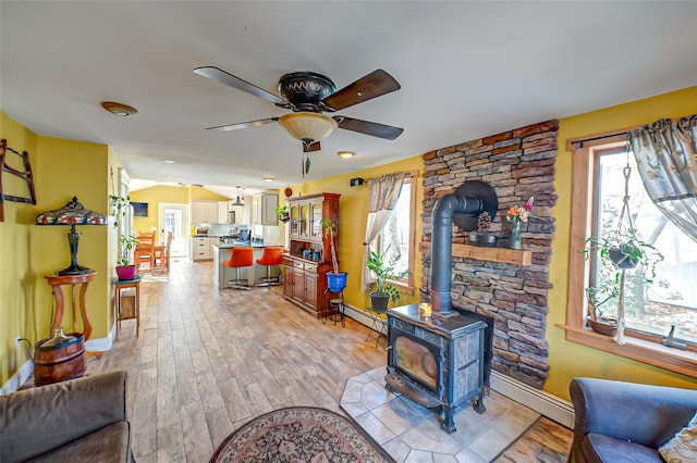 living area featuring a wealth of natural light, light wood-style flooring, a wood stove, and a ceiling fan