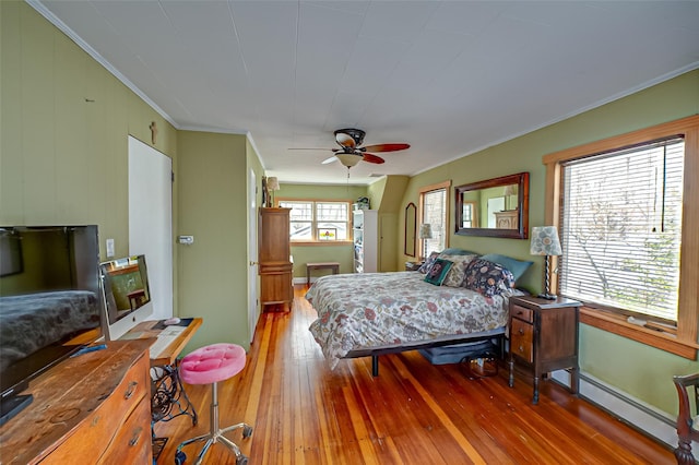 bedroom featuring a ceiling fan, wood-type flooring, a baseboard heating unit, and crown molding