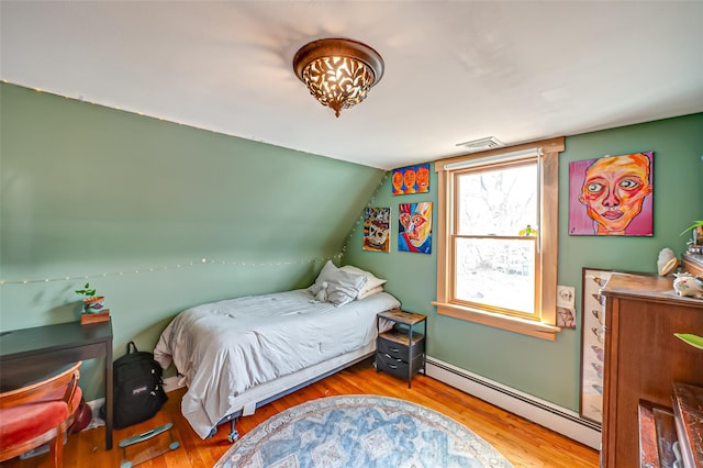 bedroom with lofted ceiling, a baseboard radiator, and wood finished floors