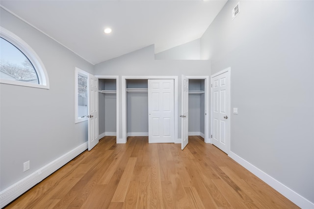 unfurnished bedroom featuring two closets, vaulted ceiling, a baseboard radiator, and light wood-type flooring