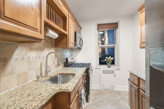 kitchen with radiator, sink, stainless steel appliances, light stone countertops, and decorative backsplash