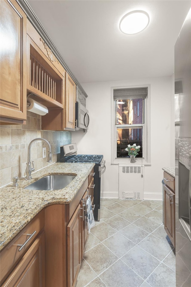 kitchen featuring radiator, sink, stainless steel appliances, light stone counters, and decorative backsplash