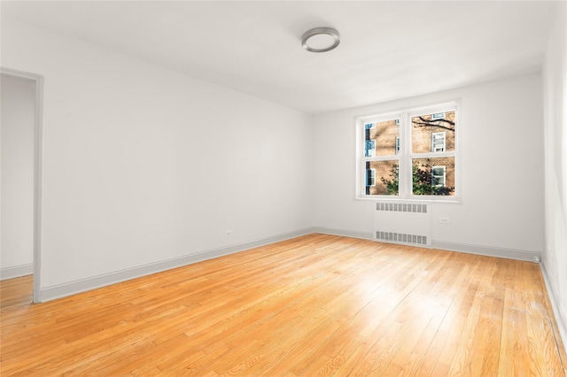 spare room featuring radiator and light hardwood / wood-style flooring