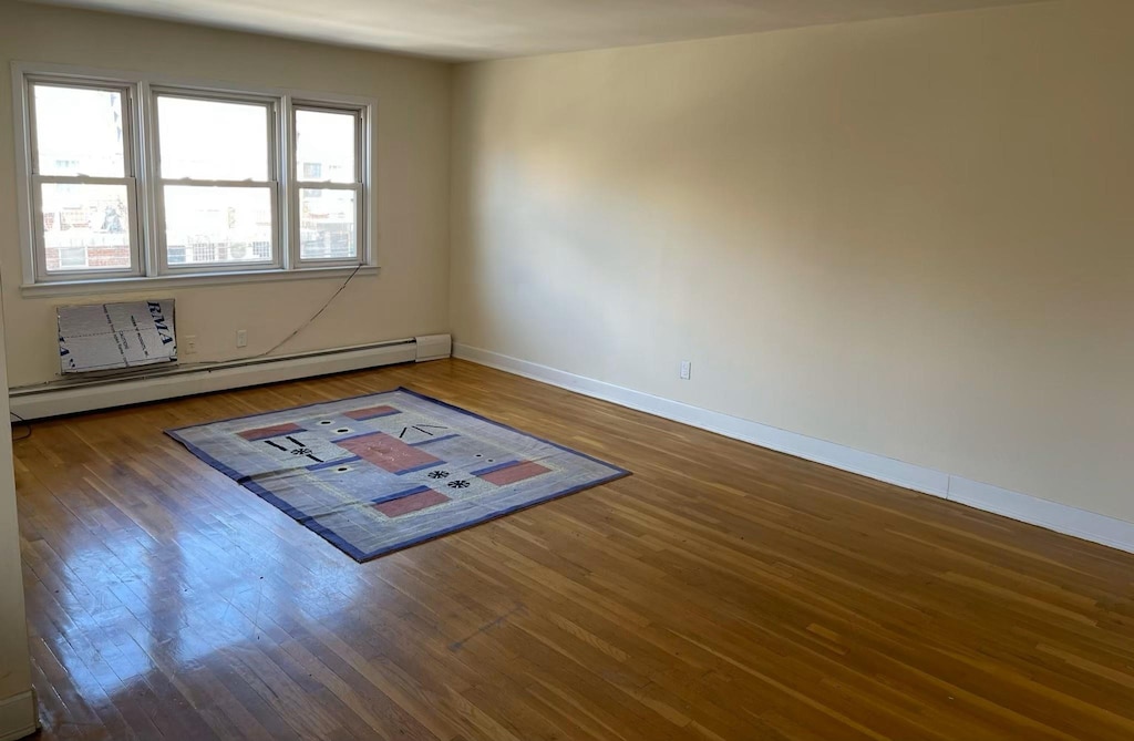 unfurnished room featuring dark wood-type flooring and a baseboard heating unit