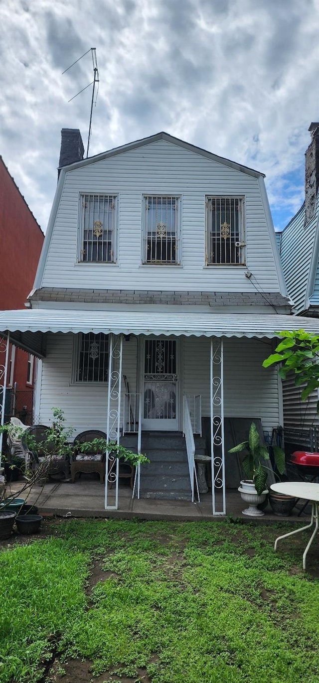 view of front facade featuring a front yard, entry steps, a chimney, and a gambrel roof