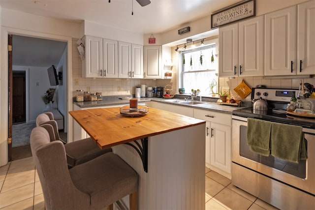 kitchen with butcher block counters, a center island, a kitchen breakfast bar, stainless steel electric stove, and white cabinets