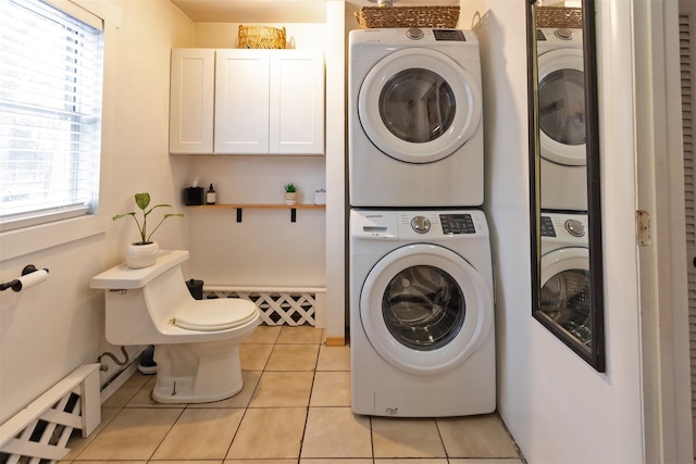 clothes washing area with baseboard heating, stacked washer and clothes dryer, and light tile patterned floors