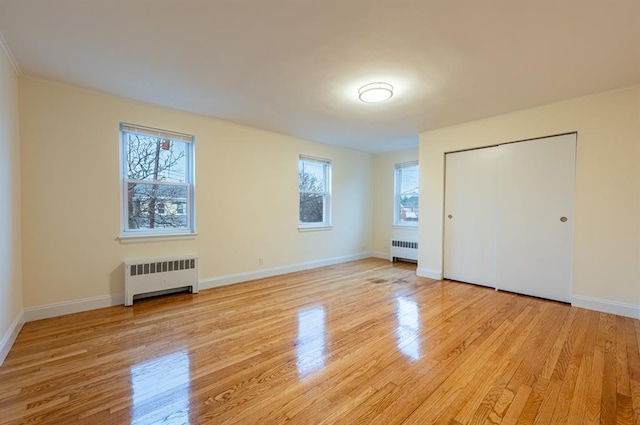 unfurnished bedroom with radiator heating unit, a closet, and light wood-type flooring