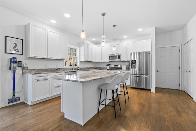 kitchen featuring white cabinetry, decorative light fixtures, a center island, dark hardwood / wood-style floors, and stainless steel appliances