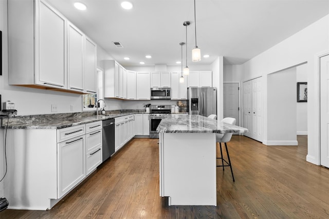 kitchen featuring a kitchen island, appliances with stainless steel finishes, pendant lighting, white cabinetry, and a kitchen breakfast bar