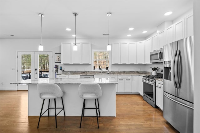 kitchen featuring stainless steel appliances, white cabinetry, a kitchen island, and decorative light fixtures