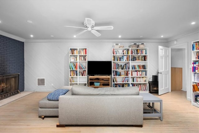 living room with ornamental molding, light hardwood / wood-style floors, a large fireplace, and ceiling fan