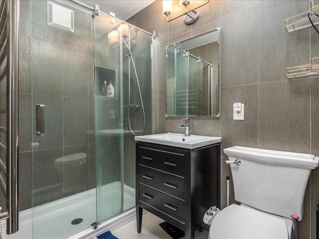 bathroom with vanity, a shower with shower door, tile walls, and toilet