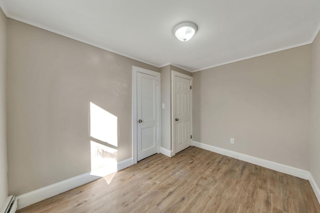 spare room featuring a baseboard radiator, ornamental molding, and light wood-type flooring