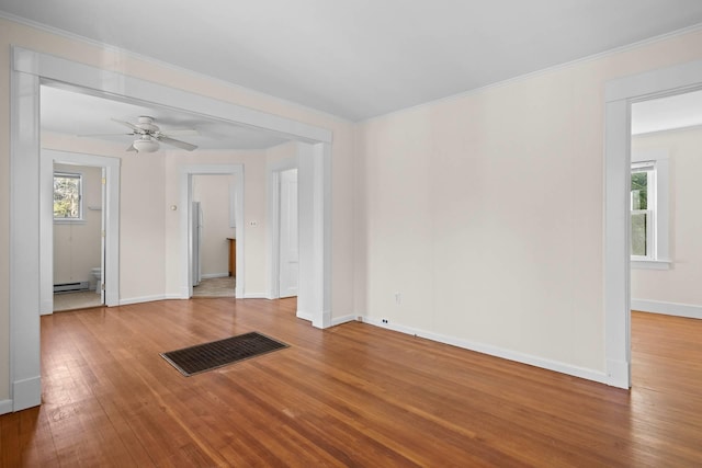 empty room with hardwood / wood-style floors, a baseboard radiator, a wealth of natural light, and ceiling fan