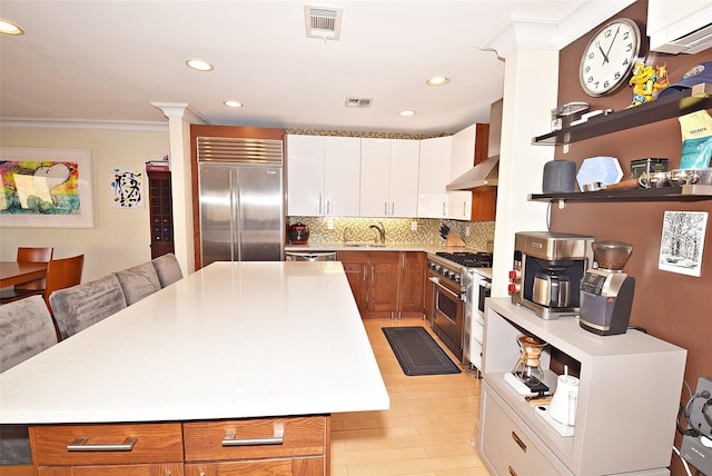 kitchen with sink, crown molding, wall chimney range hood, a center island, and high end appliances