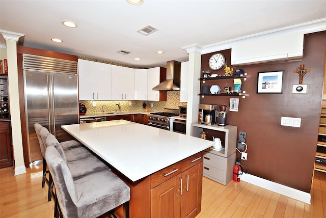 kitchen featuring sink, high end appliances, a center island, a kitchen breakfast bar, and wall chimney range hood