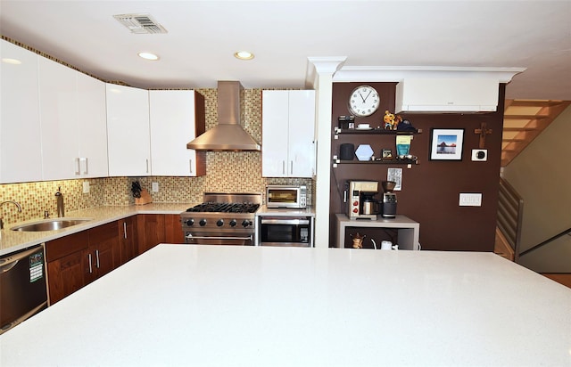 kitchen featuring appliances with stainless steel finishes, sink, white cabinets, decorative backsplash, and wall chimney exhaust hood