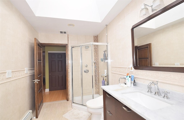 bathroom featuring a skylight, tile walls, vanity, toilet, and a shower with door