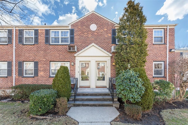 view of front of property with entry steps, an AC wall unit, brick siding, and french doors