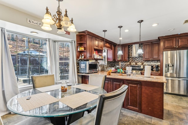 kitchen featuring appliances with stainless steel finishes, hanging light fixtures, tasteful backsplash, light stone counters, and wall chimney exhaust hood