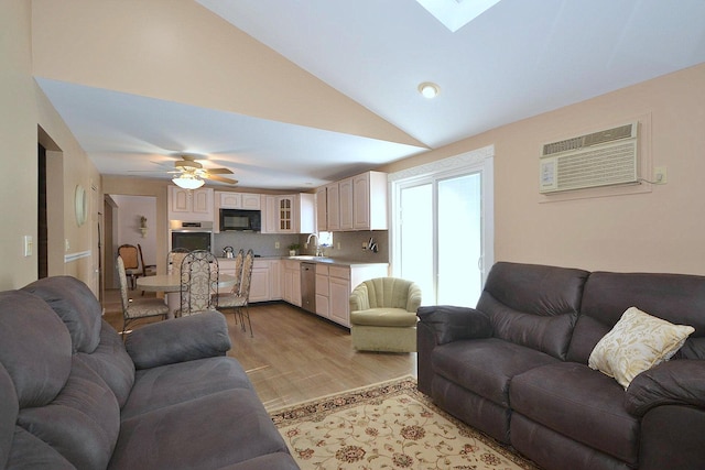 living room with sink, light hardwood / wood-style flooring, a wall unit AC, ceiling fan, and vaulted ceiling with skylight