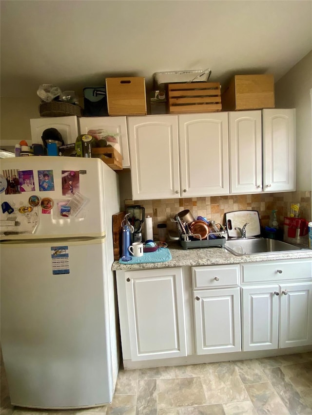 kitchen with white refrigerator, white cabinetry, sink, and decorative backsplash