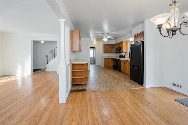 kitchen featuring pendant lighting, ceiling fan with notable chandelier, light hardwood / wood-style flooring, and black appliances