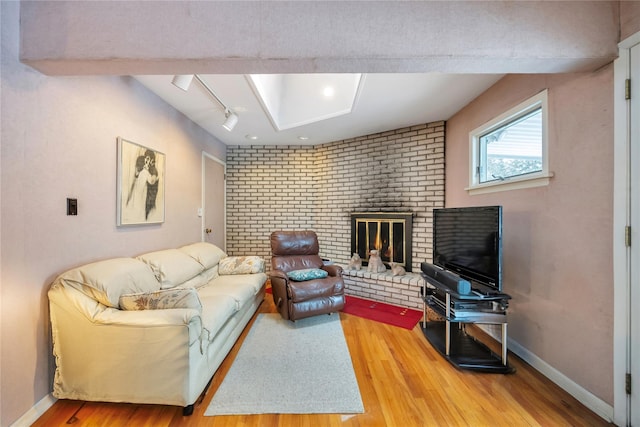 living room with a brick fireplace, hardwood / wood-style floors, rail lighting, and brick wall