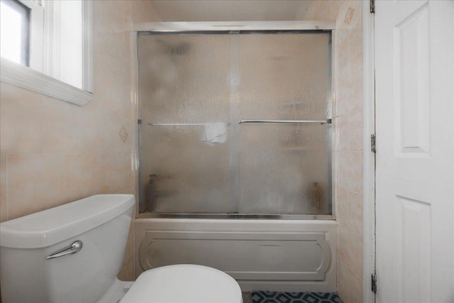 bathroom with enclosed tub / shower combo, toilet, and tile walls